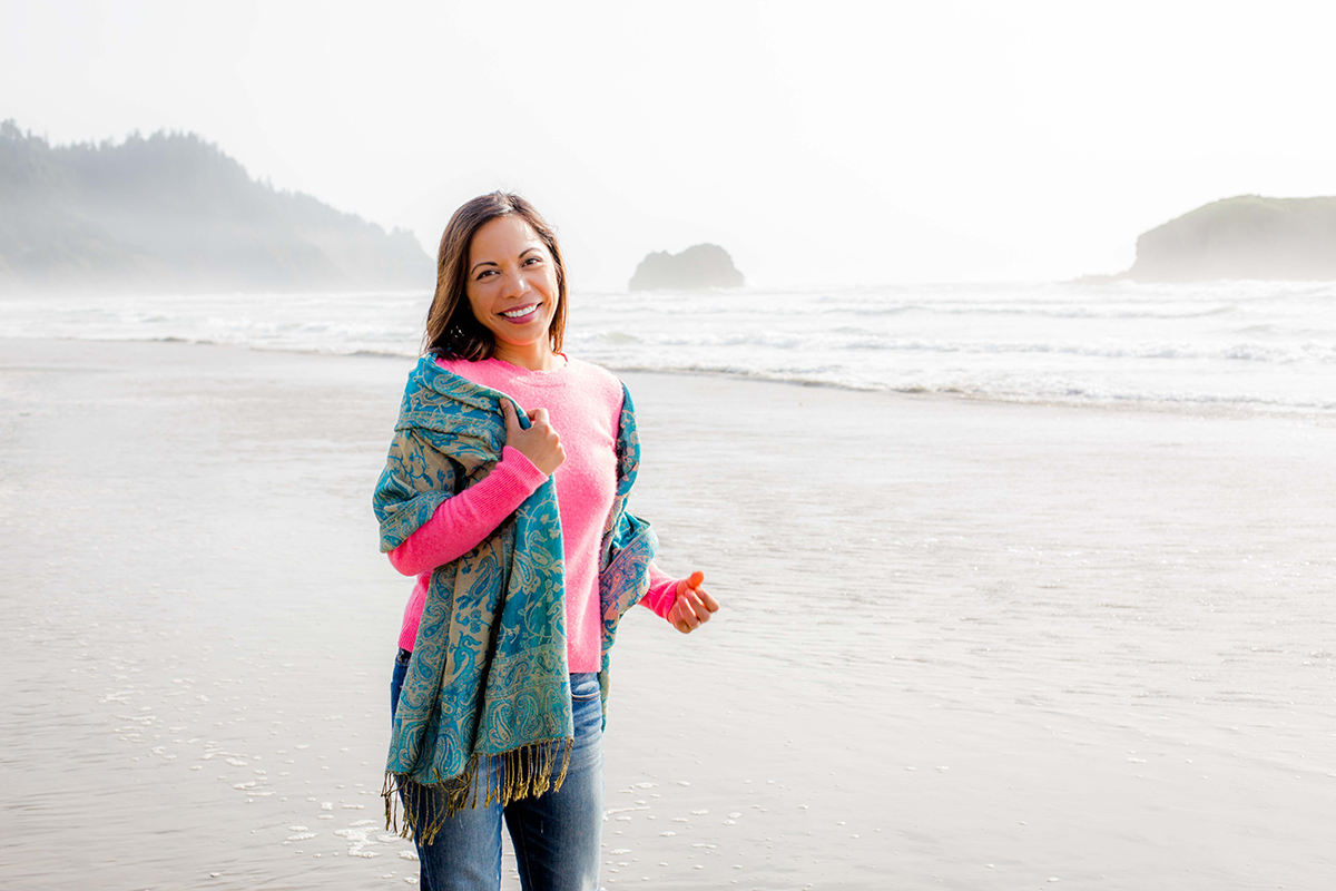 Ruby Somera in a pink sweater standing on the beach at the Oregon Coast